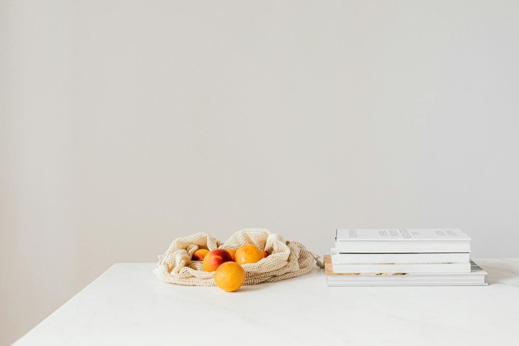 Jute sack with natural ripe apricots on white table composed with stack of various books and magazines