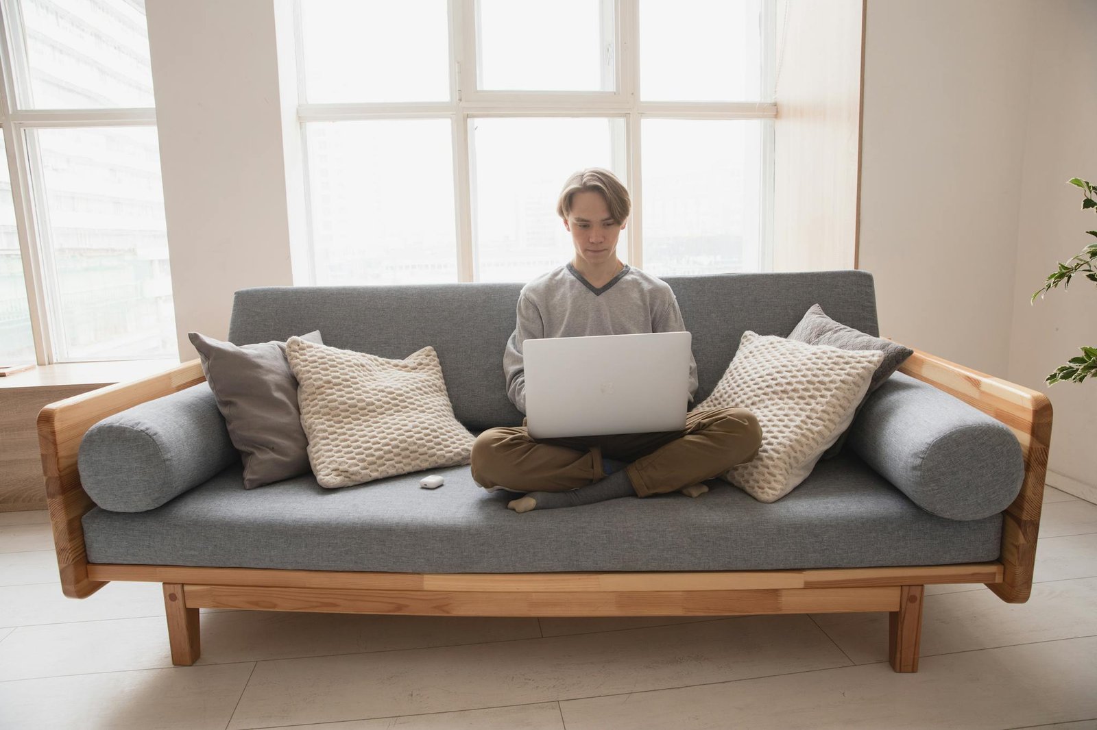 Young man working from home on a laptop, sitting comfortably on a modern couch.