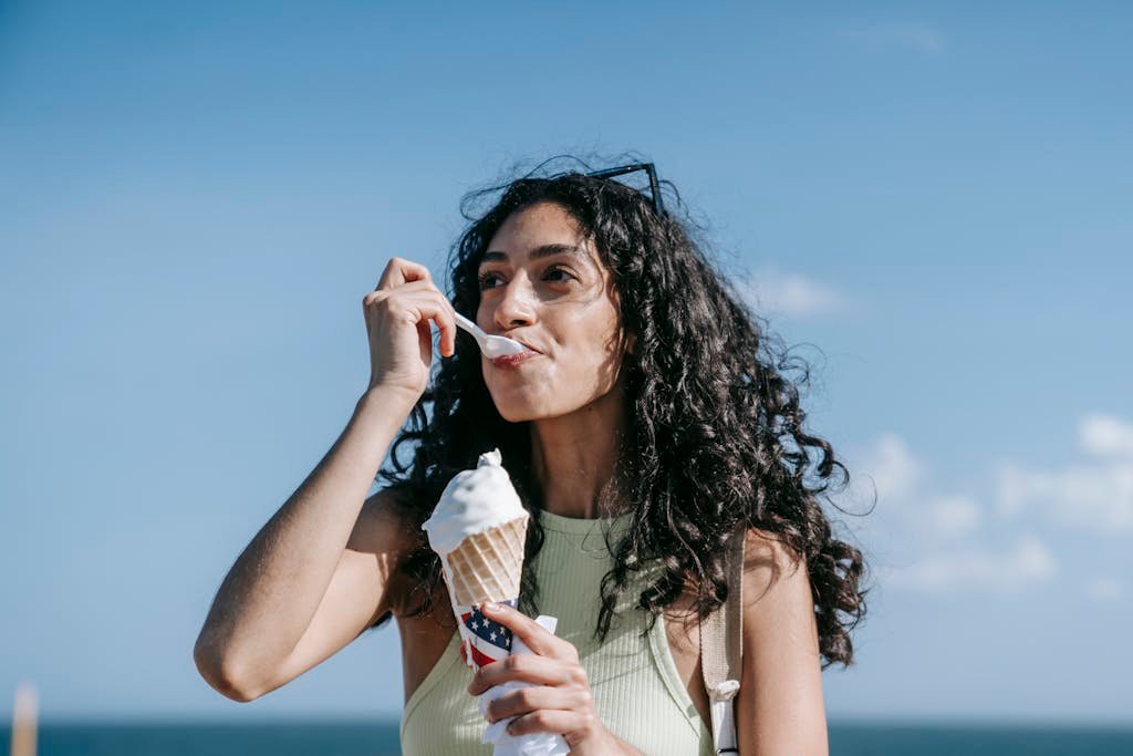 A woman savors an ice cream cone outdoors against a clear blue summer sky.