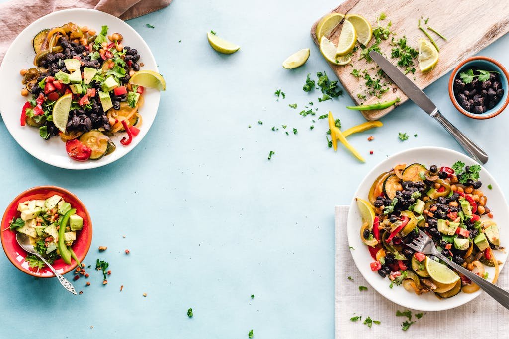 Colorful Mexican salad with avocado, black beans, and lime on a light blue surface.