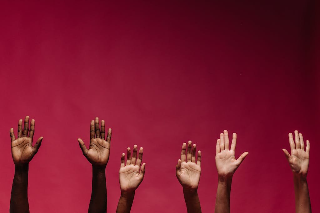 Image of diverse raised hands against a vibrant red background, symbolizing unity and diversity.