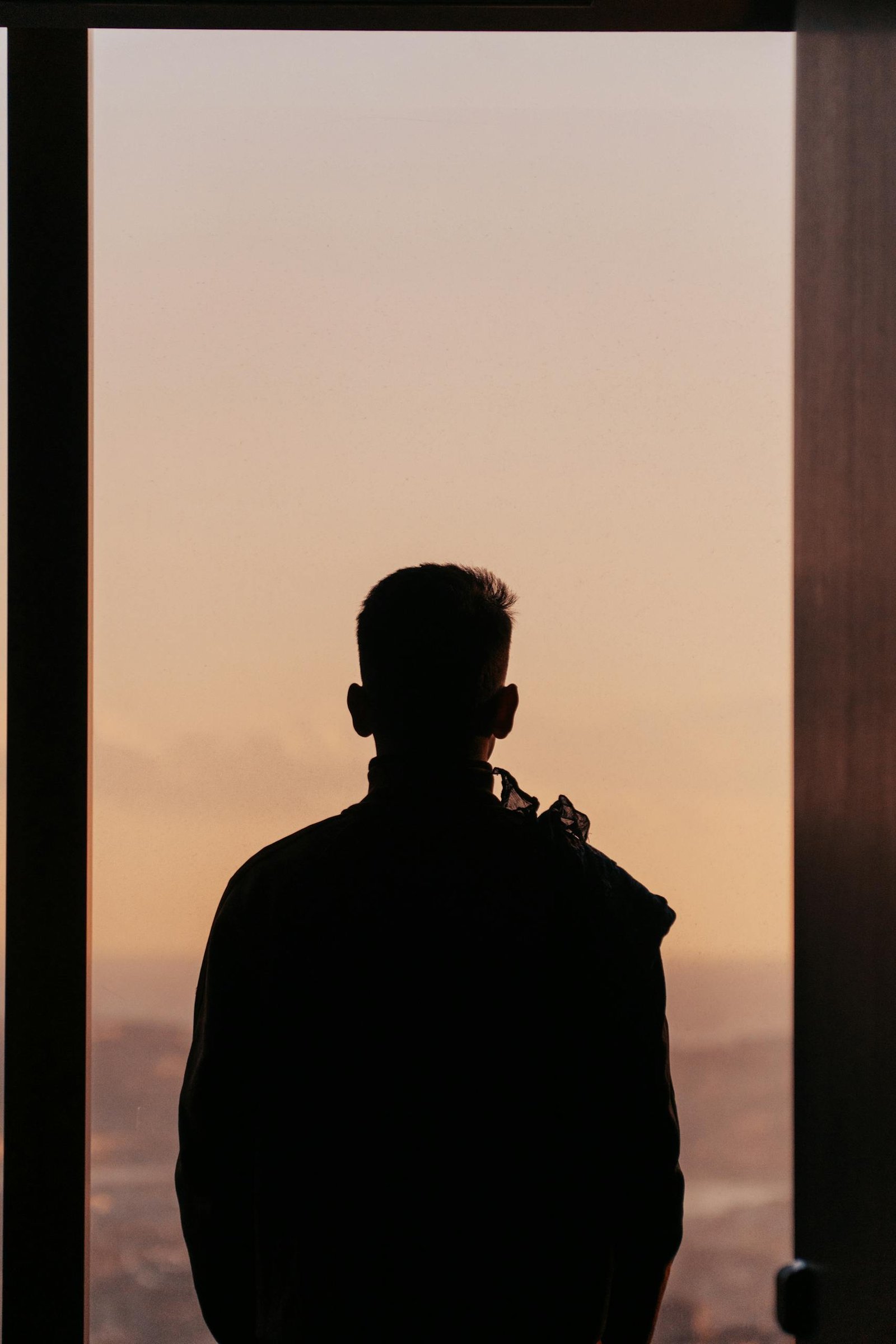 Silhouette of a man gazing out a window, capturing the serene sunset sky.