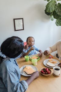 A family enjoying a breakfast of scrambled eggs and pancakes together indoors.