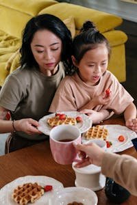 Mother and daughter having a cozy breakfast with waffles and strawberries indoors.