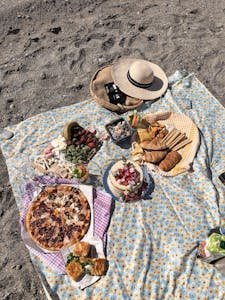 A vibrant beach picnic with assorted snacks and pizza on a sunny day in Turkey.