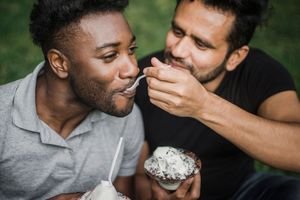 Two men happily sharing ice cream, enjoying a sunny day together.